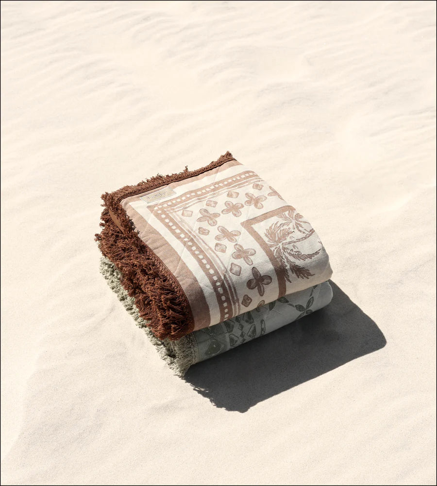 Two Layday blankets with brown and beige patterns on a sandy surface