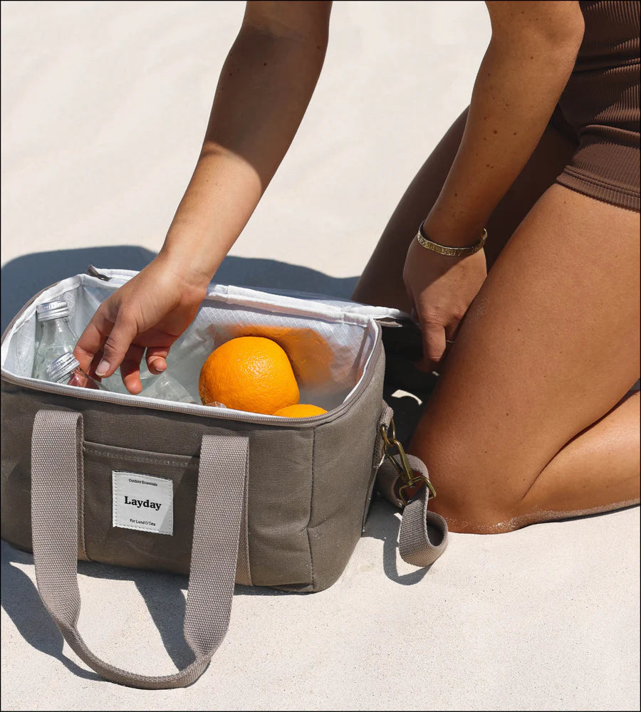 Person opening a Layday cooler bag containing oranges on a sandy surface.