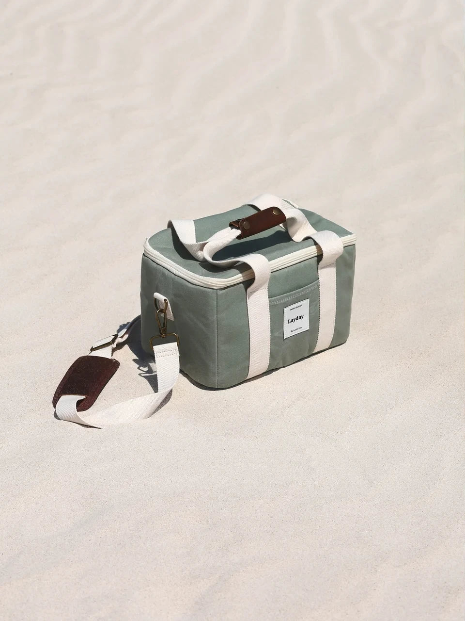 Green Layday cooler bag with a white strap on a sandy surface.