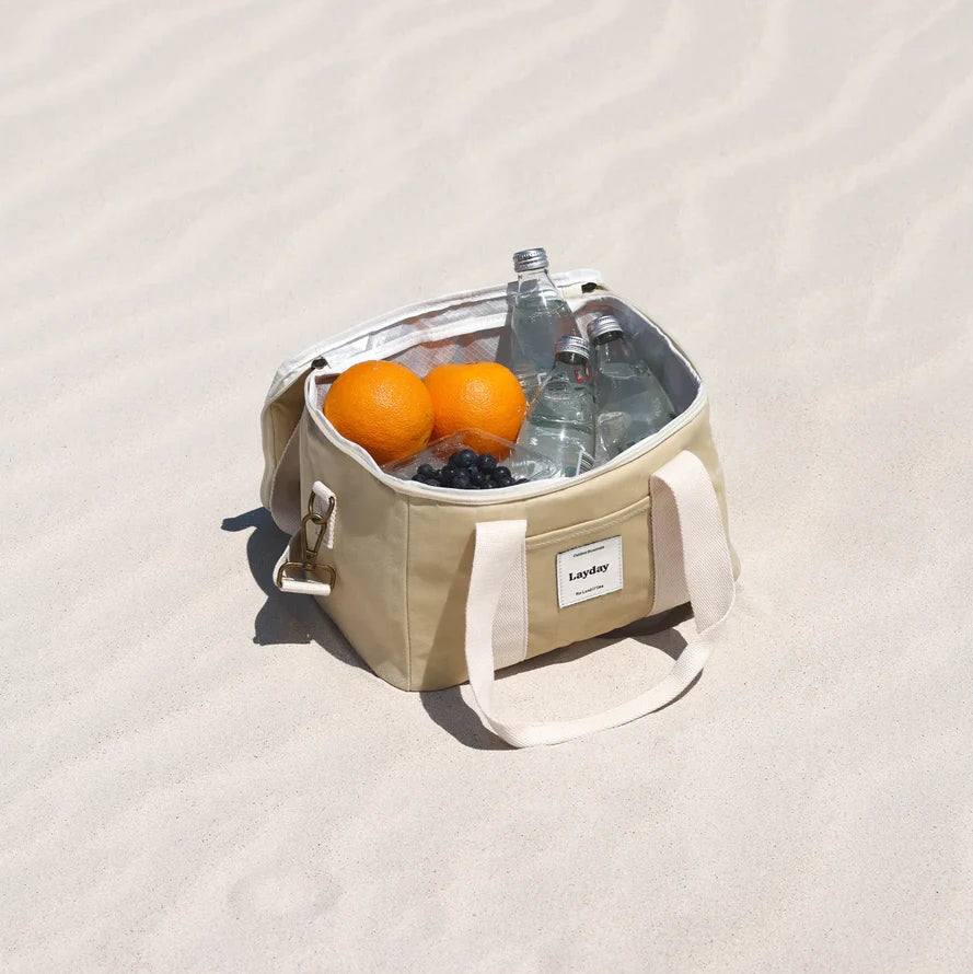 Beige Layday cooler bag with oranges, bottles, and ice on a light beige background