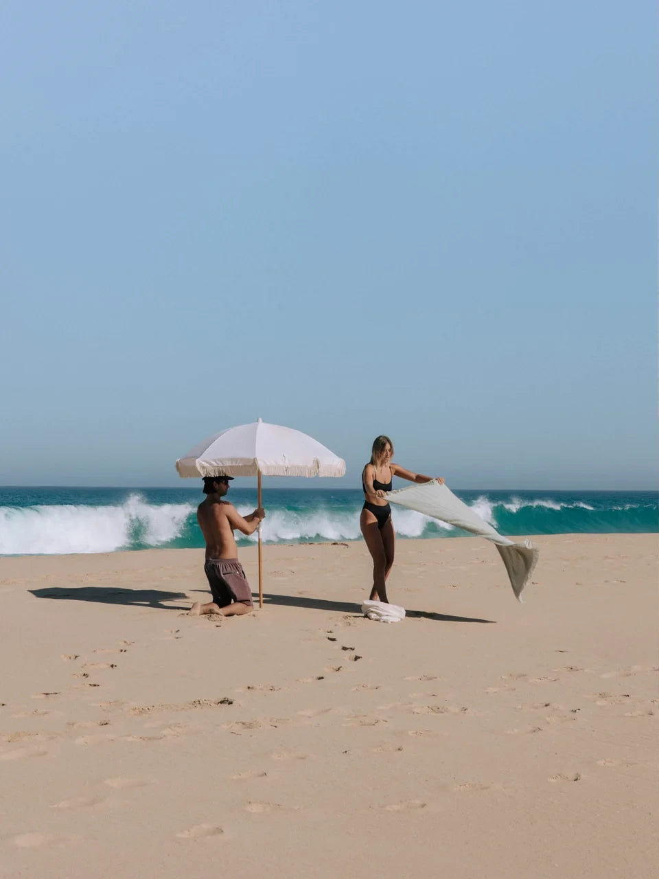 Two people on a beach with a Layday umbrella and towel