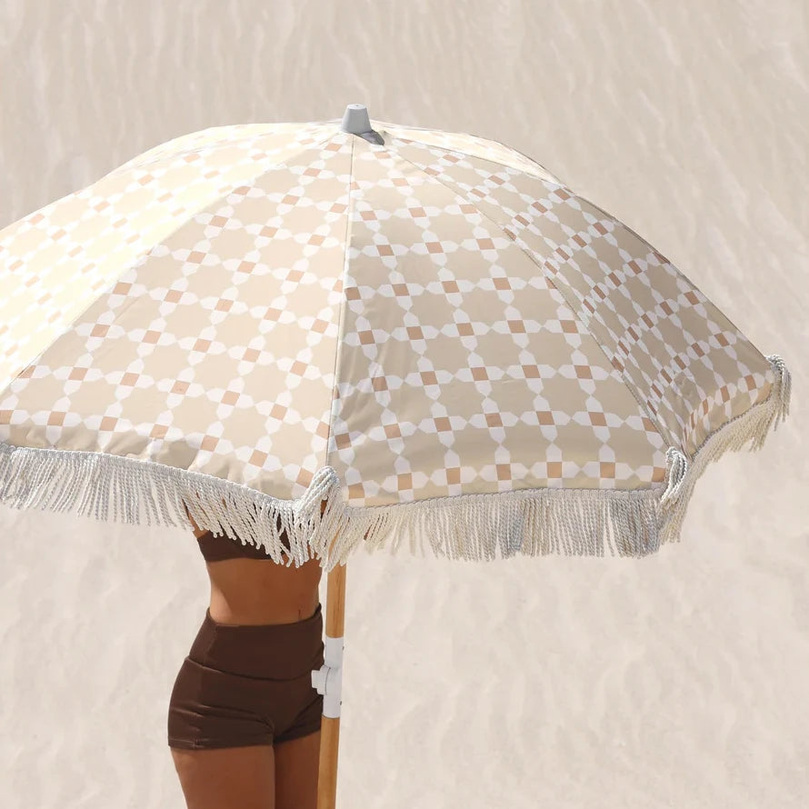 Beige checkered Layday beach umbrella with fringe on a sandy background
