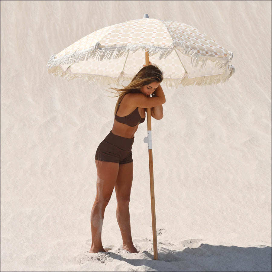 Woman in a brown bikini standing on a sandy beach with a decorative Layday umbrella.